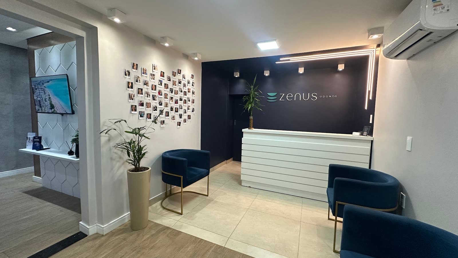 Recepção da Zenus Odonto: parede azul com o logo, balcão branco de frisos, poltronas de veludo azul e o mural com fotos dos pacientes